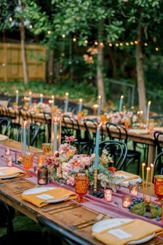 a long table with candles and flowers on it is set up for an outdoor dinner