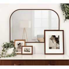 a couple kissing in front of a large mirror on top of a dresser next to two framed photos