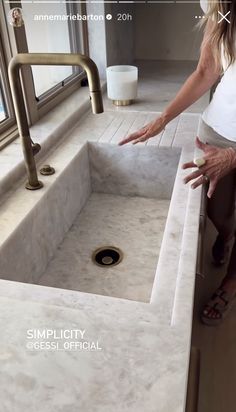 a woman standing in front of a sink with her hand on the faucet