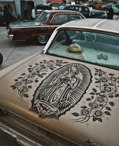 an old car parked on the side of the road with a virgin mary tattoo on it's hood