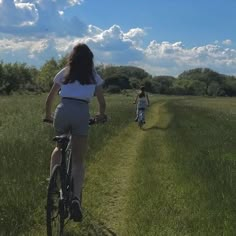 two people riding bikes on a dirt path in the middle of an open field with tall grass