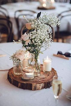 flowers and candles are arranged in mason jars on a wooden slice at a wedding reception