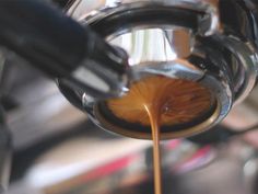 coffee being poured into a cup on top of a machine with liquid pouring out of it