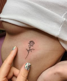 a woman's stomach with a small rose tattoo on her left side ribcage