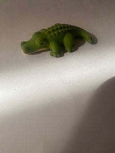 a small green toy alligator laying on top of a white sheet with shadow coming from it