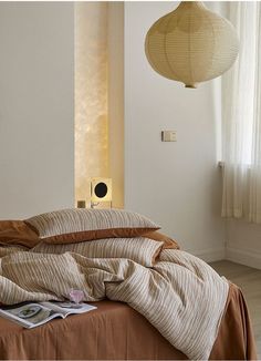 an unmade bed in a white room next to a lamp