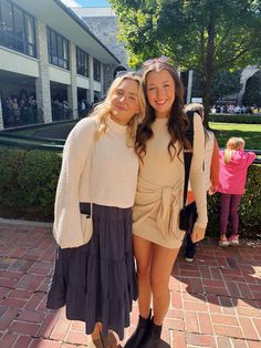 two young women standing next to each other on a brick walkway in front of a building