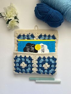 a crocheted purse with blue and white flowers on it next to a ball of yarn