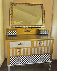 a dresser with checkered drawers and a mirror on it's top, in front of a wall