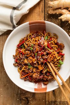 a bowl filled with noodles and vegetables on top of a wooden table next to chopsticks