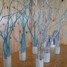 several vases with branches in them sitting on a wooden table next to a wall