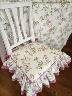 a white chair with pink and green flowers on it's seat cover next to a bed