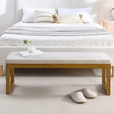 a white bed sitting next to a wooden footstool on top of a carpeted floor