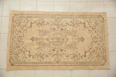 an old rug is laying on the floor in front of a white tile wall,