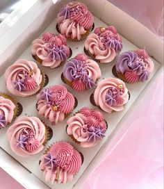 twelve cupcakes with pink frosting and purple icing in a white box