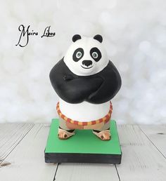 a cake shaped like a panda bear sitting on top of a green base with its arms crossed