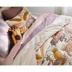 an unmade bed with pink and purple comforter, pillows and stuffed animals on it