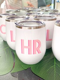 white wine glasses with pink lettering on them sitting on a green leafy table top