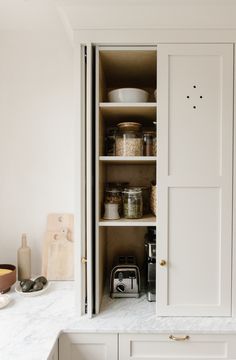 an open cabinet in the middle of a kitchen with white cupboards and counter tops