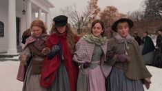 four women in long dresses and hats are standing outside in the snow with their arms around each other