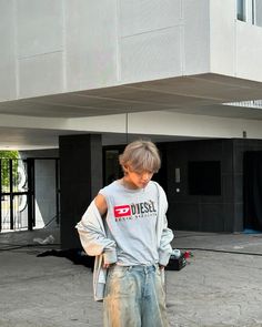 a man standing in front of a building with his back to the camera, wearing jeans and a t - shirt that says diesel