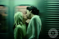 a man and woman kissing in front of a subway train as it passes by them