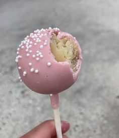 a hand holding a pink cake pops with white sprinkles