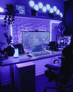 a desk with a computer and speakers on it in front of a purple wall that has hexagonal lights