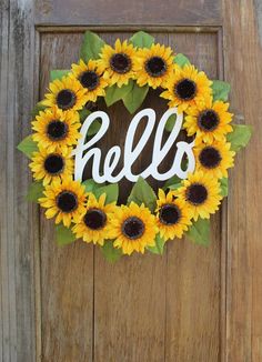 a wreath with the word hello painted on it and sunflowers in front of a wooden door