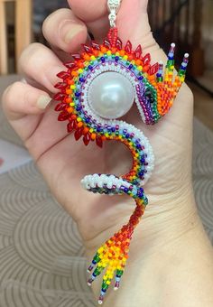 a person holding up a colorful beaded dragon brooch and pearl necklace in their hand