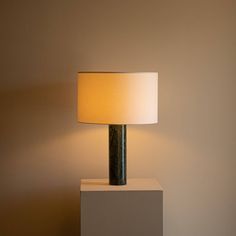 a table lamp sitting on top of a white block next to a light brown wall