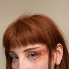 a close up of a person with red hair and gold paint on her face, wearing earrings