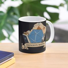 a coffee mug sitting on top of a wooden table next to a book and plant