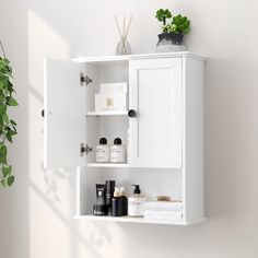 a white cabinet with some plants and other items on it's shelf next to a potted plant