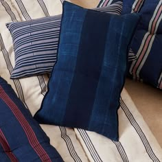 three pillows on top of a bed with blue and red striped sheets in the background