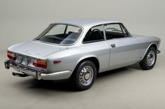 an old silver car is parked on the floor in front of a white wall and grey background