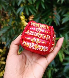 a hand holding a small red case in front of some trees