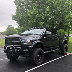 a black ram truck parked in a parking lot next to a large green leafy tree