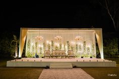 an outdoor stage set up for a wedding with chandeliers and flowers on it