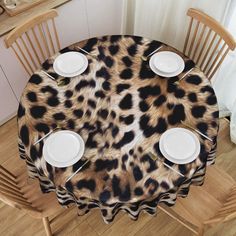 an animal print table cloth with white plates on it and wooden chairs around the table