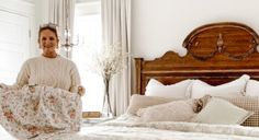 a woman standing in front of a bed holding a blanket