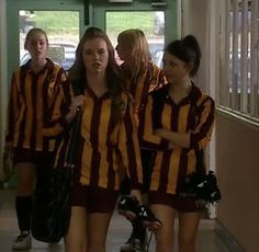 the girls are walking down the hall together in uniforms and holding baseball mitt's