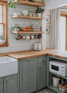 a kitchen with green cabinets and wooden counter tops, white tile backsplash and open shelving above the sink