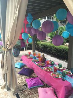 a table set up for a party with paper lanterns hanging from the ceiling and plates on it