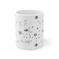 a white coffee mug with space drawings on it's side and stars in the sky