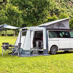 a camper van is parked in the grass with its door open and it's awning opened