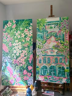 two paintings on easels in front of a window with flowers and plants painted on them