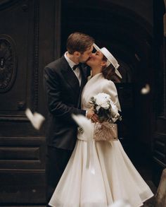 a bride and groom kissing in front of a building with pigeons flying around their heads