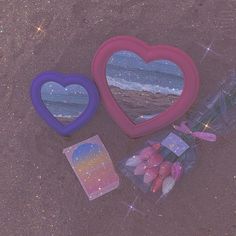 three heart shaped mirrors sitting on top of a sandy beach next to a bag of candy