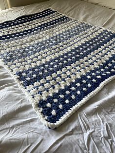 a crocheted blue and white blanket laying on top of a bed